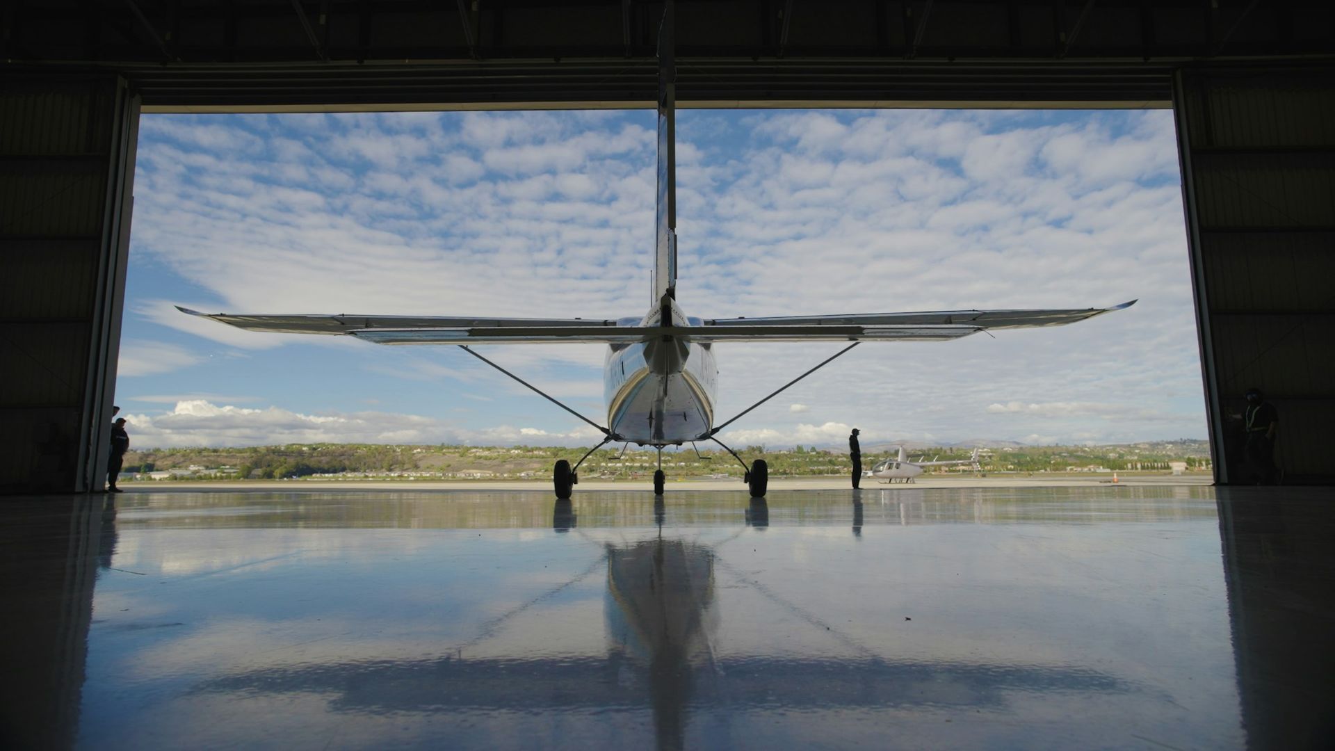 Monomoteur à aile haute dans l'ouverture d'un hangar, reflet au sol